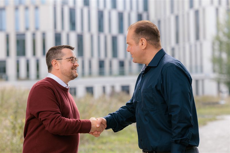 Martin Höschler und ein Gesprächspartner geben sich vor einem Neubau die Hand
